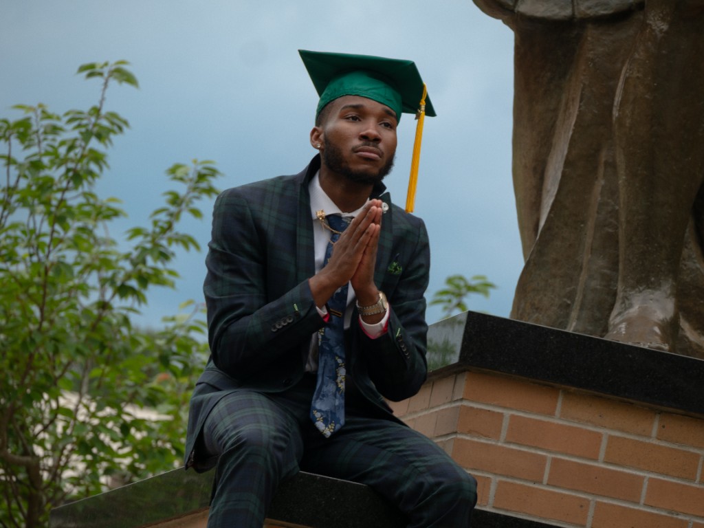 Graduate seated near statue in dark plaid suit