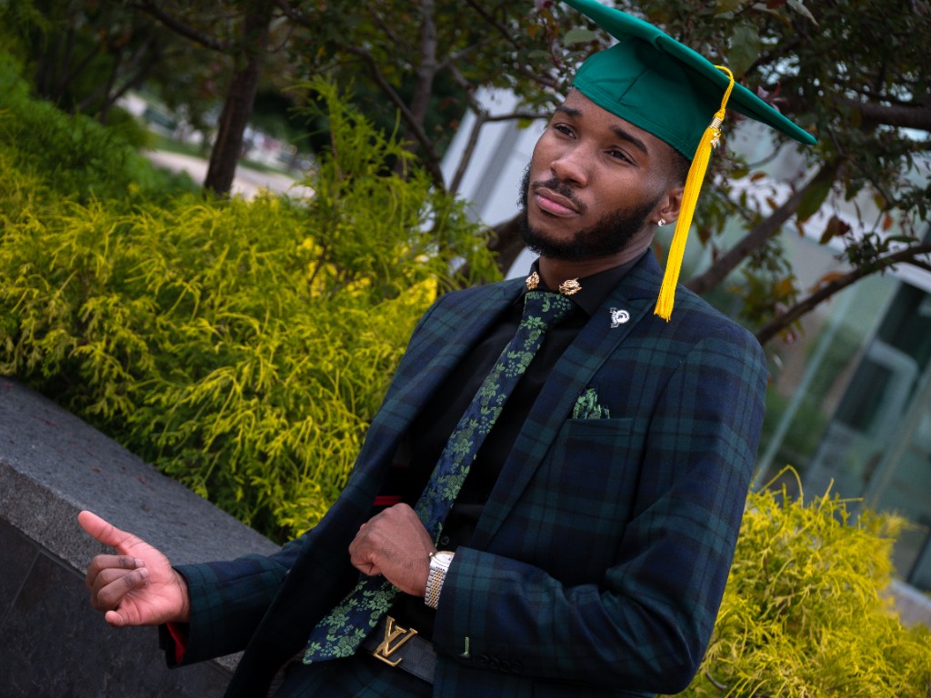 Graduate portrait in dark suit with greenery backdrop